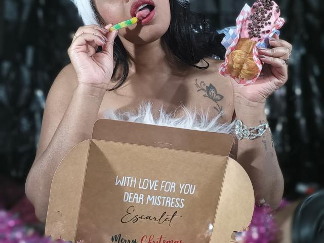 DeborahDeluxe, avec ses cheveux foncés, la langue tirée, léchant un bonbon, tenant des beignets, portant une fourrure blanche, avec des tatouages et un bracelet à motifs léopard, tenant une boîte marron..