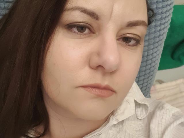 AnnaFock has a pensive, slightly annoyed expression with brown eyes, light skin, and brown hair. She's wearing a white shirt, and a blue textured headband is in the background.