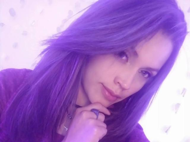 LinaStars with purple hair, a slight smile, and a ring on her finger, touching her chin, looking cute. Her tits are not visible, just her face and hand.