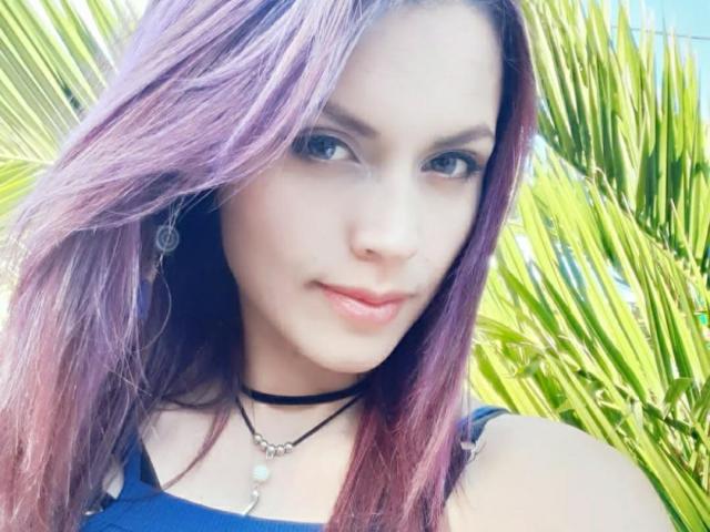 LinaStars has purple hair, blue eyes, and a cute face with pink lips. She's wearing a black choker and blue top, with green palm leaves in the background.