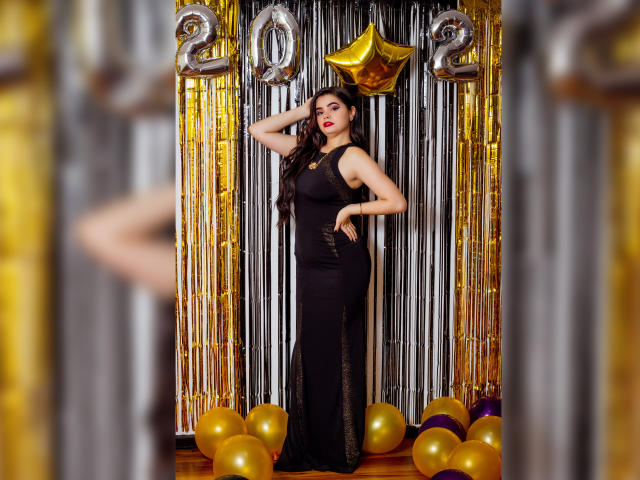 BrithneyLee mit langen, dunklen Haaren in einem schwarzen Kleid, steht mit einer Hand auf dem Kopf, umgeben von goldenen Ballons und silbernen Girlanden, mit einem goldenen Stern und Ballons mit der Aufschrift "20"..