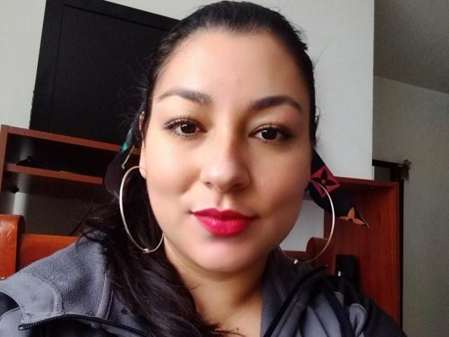 SakotoDika tiene la piel de color marrón medio, cabello oscuro recogido en una coleta, aros grandes y un lápiz labial rosa brillante. Lleva una chaqueta gris y mira a la cámara con una ligera sonrisa..