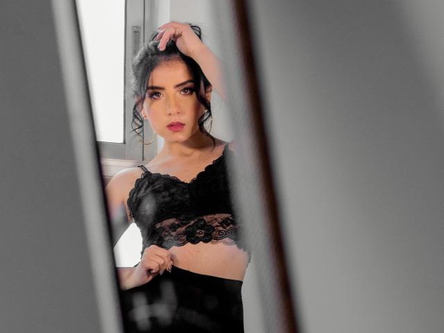 Kathy Rosse mit dunklem Haar, in einem schwarzen Spitzen-BH, die durch ein Fenster schaut, eine Hand im Haar, weiches Licht, Halbnahaufnahme, dezentes Make-up, leichtes Schmollen, kleine Brüste, selbstbewusster Ausdruck..