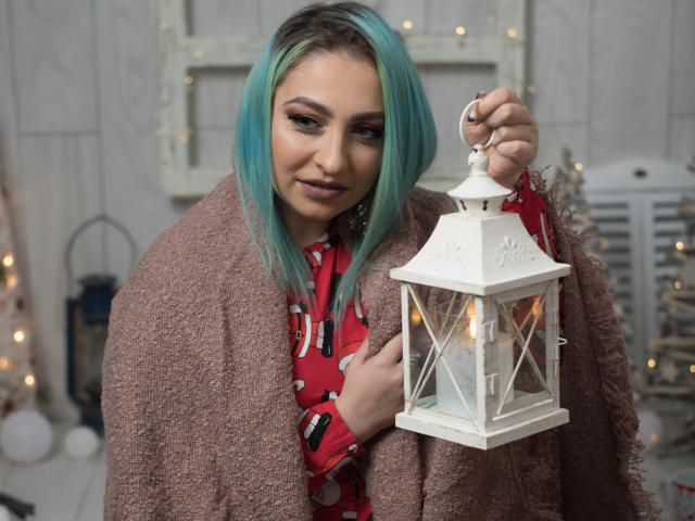 Agaa with blue-green hair, red patterned shirt, and pinkish-brown shawl, holding a white lantern with lit candles, looking down with a subtle smile. Boobs covered by shawl.