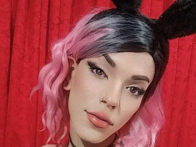 LucyVendeta con capelli ondulati rosa e neri, orecchie da coniglio nere e labbra piene rosa, che guarda la fotocamera con occhi marroni e sopracciglia arcuate, indossando una collana nera..