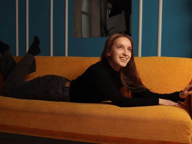 EvaPink lying on a yellow sofa, black turtleneck, dark jeans, black socks, smiling, brown hair, blue eyes, hands on sofa, legs bent, butt up, casual, sexy.