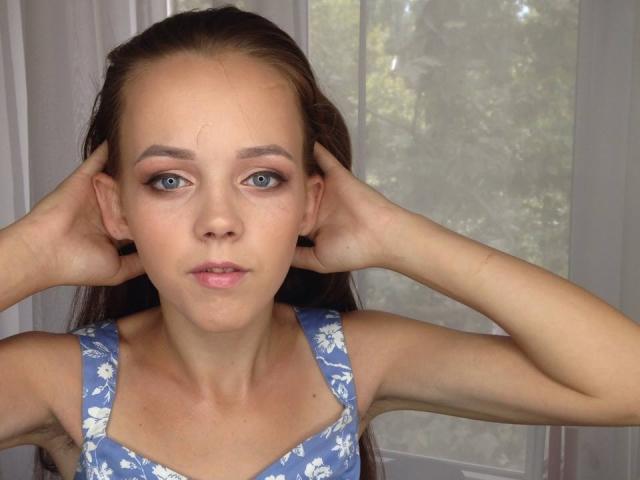 JeannieTina with hands in brown hair, blue floral dress, pale skin, blue eyes, pink eyelids, slightly parted pink lips, looking forward, soft natural light.
