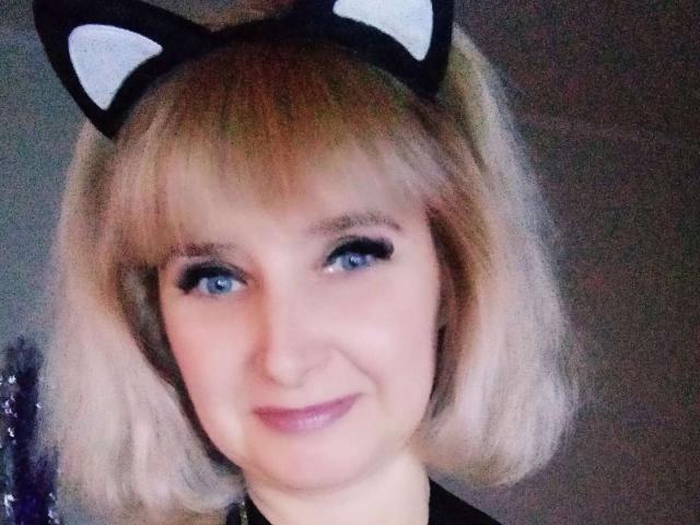 VAlica has blonde bob, blue eyes, black cat ears, and a subtle smile, wearing black eyeliner, and a black top. Her pink lips are slightly parted.