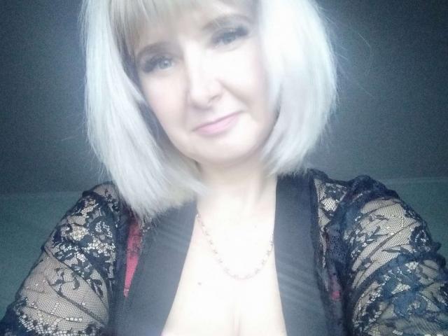 VAlica with white bob, black lace top, exposing cleavage, slight smile, light skin, subtle makeup, necklace, soft light, semi-sheer fabric, casual selfie.