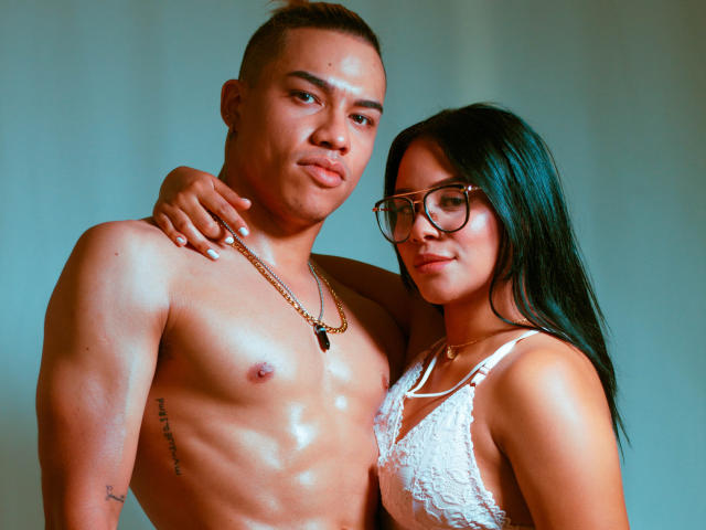 HoneyAndMaky, een blanke man met een tatoeage en een gouden ketting, staat met zijn arm om een schattig Aziatisch meisje met een bril en een witte kanten beha. Ze heeft borsten..