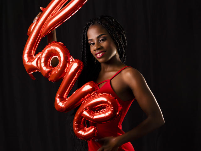 Mia Hopson mit glänzenden roten Ballons, die sie an ihrer Brust und ihrem Hintern hält, trägt ein rotes Kleid, dunkler Hintergrund, lächelnd, lange schwarze Zöpfe, Studioaufnahme..