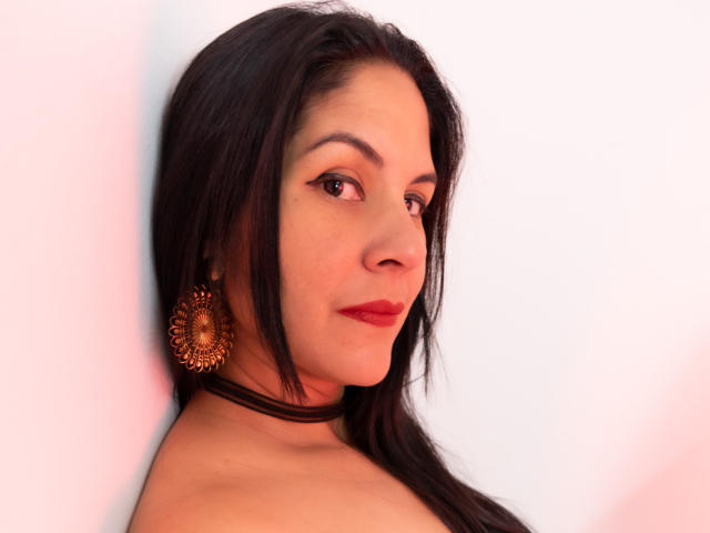 RoraimAnaggie a les cheveux foncés, du rouge à lèvres, et un regard sûr. Elle porte un collier noir et de grandes boucles d'oreilles en or, et ses épaules sont dénudées. Ses seins ne sont pas visibles..