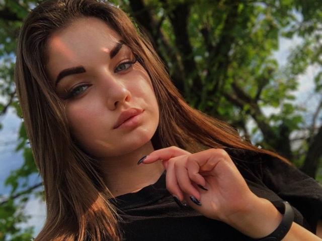 barbiandken mit braunen Haaren, grünen Augen und schwarzen Nägeln, trägt ein schwarzes Hemd, blickt in die Kamera, Sonnenlicht im Gesicht, Hand in der Nähe des Kinns, trägt eine schwarze Uhr..