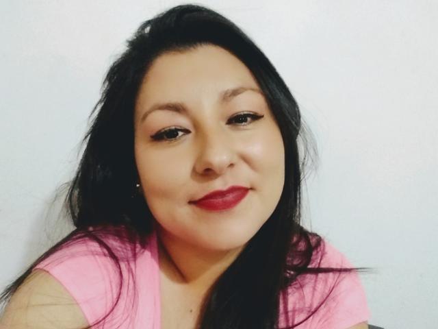 SakotoDika with long black hair, pink shirt, red lipstick, and slight smile, looking at camera, soft makeup, light skin, slightly chubby face, subtle eyeliner, relaxed expression.