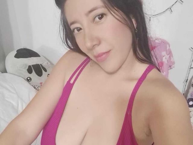 HotPamelaSex with pale skin, brown eyes, and pink lipstick, wearing a low-cut magenta top, showing her big tits and slight cleavage, with dark hair and a subtle smile.