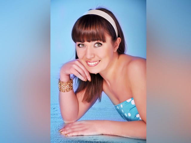 MadonyJoe, com cabelo castanho, faixa branca na cabeça, sorrindo, mostrando os seios em uma blusa branca, agachada, com os joelhos levantados, olhos verdes, fofa, atraente, fundo branco, foto de estúdio..