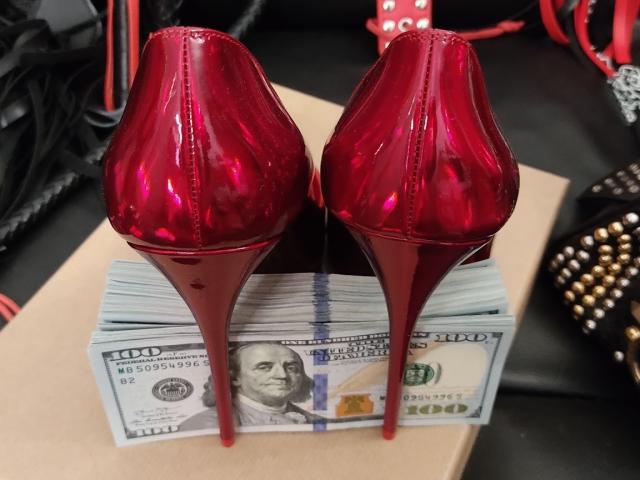 Des talons hauts rouges et brillants posés sur une pile de billets de cent dollars, avec une ceinture noire et rouge ornée de clous en arrière-plan, illustrant un décor à la fois séduisant et opulent..