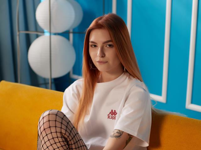 MalenaGolden met lang rood haar, een witte Adidas T-shirt, netkousen, een tatoeage op haar arm, zittend op een gele bank, een blauwe muur, witte papieren lantaarns, een subtiele glimlach, sexy, zelfverzekerd..