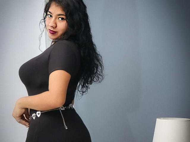 KendallOwens with curly black hair, wearing a tight black top and belt, showing her big ass and small waist, looking back with dark red lipstick.