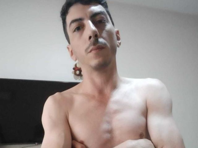 Shirtless XSantyX with crossed arms, medium build, light skin, short black hair, small mustache, looking down, bare chest, slight muscle definition, simple room background.