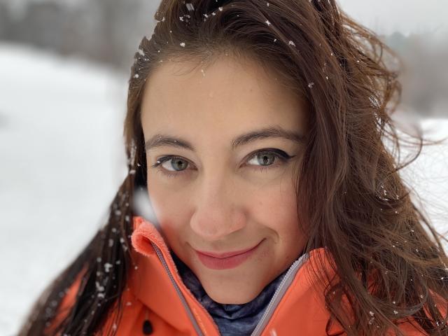 Arleen Hunter heeft groene ogen, bruin haar en een lichte glimlach, met een beetje sneeuw op haar gezicht. Ze draagt een oranje jas met een blauw shirt eronder..