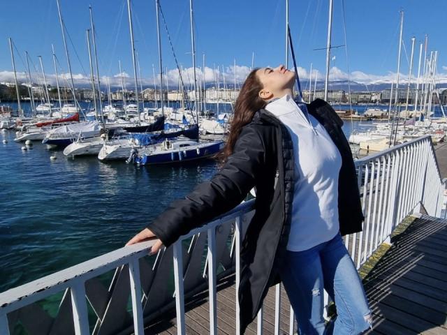 Arleen Hunter è appoggiata a una ringhiera, con gli occhi chiusi e la testa inclinata all'insù, indossa una giacca nera, una camicia bianca e jeans blu, con delle barche e un cielo azzurro limpido sullo sfondo..