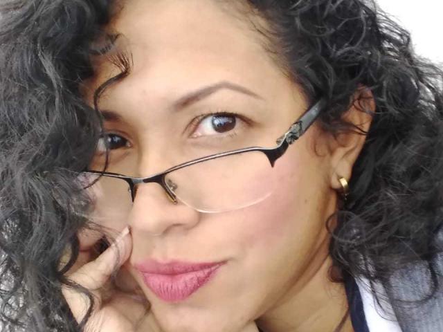 OdedySexy tiene el pelo negro y rizado, ojos marrones y usa gafas con monturas negras delgadas. Lleva lápiz labial rosa y un arete de oro, y toca su mejilla con los dedos..