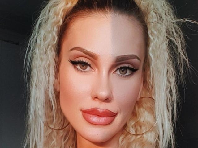 Mojoo heeft blond krullend haar, groene ogen, dikke wenkbrauwen en rode lippenstift met opvallende eyeliner. Ze draagt grote oorringen. Haar huid is licht. Ze kijkt naar de camera..