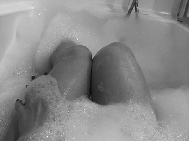 LeaLovely's legs are in a bubbly bathtub, her knees up, with her hands partially submerged, showing off her ass and slightly visible pussy under the foam.
