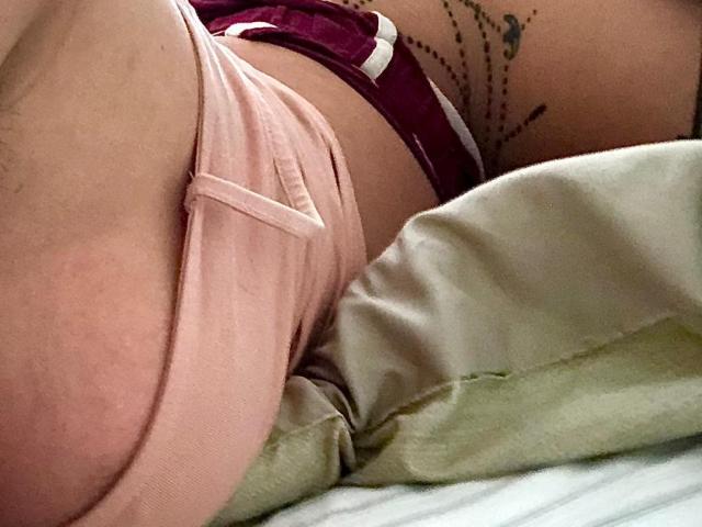 ElianMoon's pink shorts, showing a bit of white underwear, with a tattoo on their side and lying on a pillow. Boobs slightly visible, ass mostly covered.