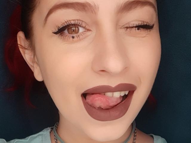 Agaa's face with one eye closed, winking. She's sticking out her tongue, showing pink tongue and brown lipstick. Her brown eyebrows are raised, and she has long eyelashes.