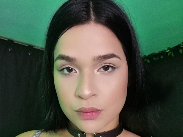 Antonela Park tiene la piel clara, cabello negro, delineador de ojos azul, labios rosados y un collar negro con un anillo de plata. Su expresión es neutra y está mirando a la cámara..