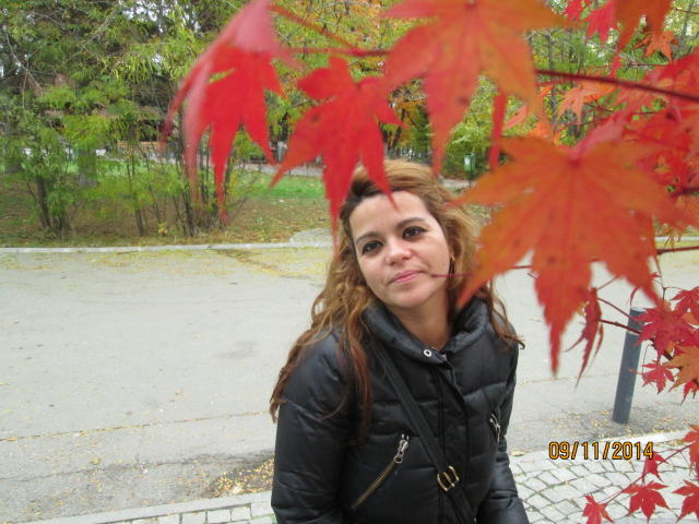 FacialEjac has curly brown hair, wearing a black puffy jacket, with red autumn leaves in the foreground. Date stamp in bottom right.