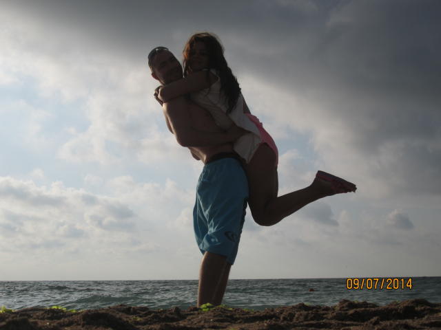 FacialEjac with a butt, holding FacialEjac with tits and a pussy, against a cloudy sky. FacialEjac is in blue shorts, FacialEjac wears pink underwear. Date watermark.