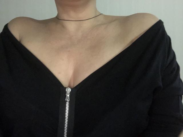 LadyMiller's chest with her tits slightly visible through a black off-shoulder zip-up, showing a metal zipper down the center. She has a thin black necklace.