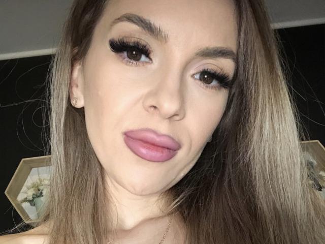 SophieDeee's face with pouty pink lips, long brown hair, and thick black eyelashes. She's staring up with a slightly goofy expression. Her tits are not visible.
