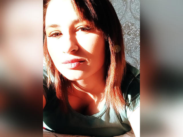 ElisionPray ha i capelli castani, la pelle chiara e le labbra rosa. Indossa una maglietta verde, con la luce del sole che illumina il suo viso. È visibile un'ombra sul seno. Lo sfondo è sfocato..