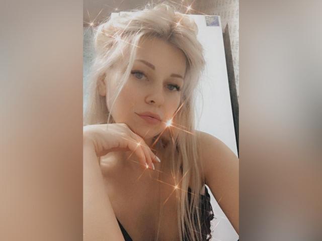 CrazyLedyi has blonde hair, light skin, and is looking at the camera with a slight smile, resting her chin on her hand. Glitter effects are added to the image.
