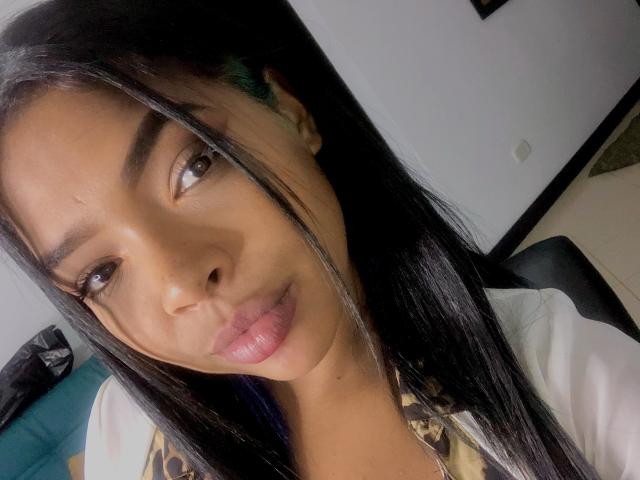 VickyGreys has long black hair, brown eyes, and glossy pink lips. She's wearing a leopard print shirt, looking at the camera with a slight smile.