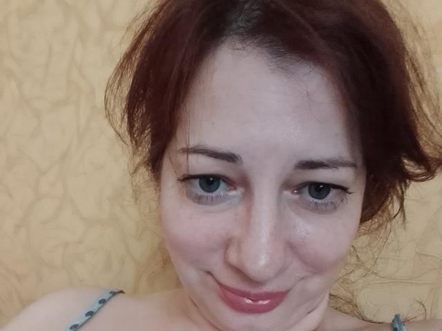 LediSusana hat helle Haut, rote Haare, die zu einem unordentlichen Dutt gebunden sind, blaue Augen und ein leichtes Lächeln mit glänzenden, rosafarbenen Lippen. Sie trägt einen blauen Träger..