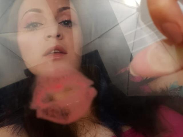 ElinaJhonson's face is in the foreground, with a blurred pink lip print and her hand with a tattoo in the background. Her pink eyeshadow and black hair are visible.