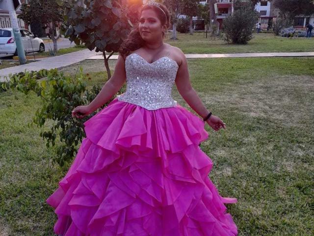 ArtemisaRoses tiene unas nalgas grandes, vestida con un vestido rosa, con volantes y sin tirantes, y con un escote blanco brillante. Está de pie sobre la hierba, llevando una tiara, con las manos bajas..