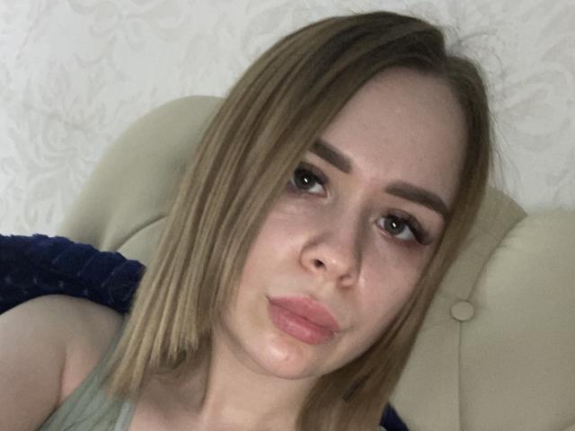 MissAprilBi has light brown hair, puffy pink lips, and thick eyebrows. She's wearing a blue top, looking slightly bored with her eyes half-open. Her boobs are partially visible.