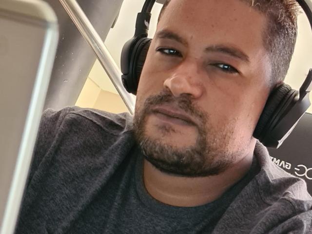 MrBlackHot, een wat dikker man met een bruine baard en kort haar, die zwarte hoofdtelefoons draagt, kijkt verveeld in een selfie met een lichtelijk bedroefde uitdrukking..