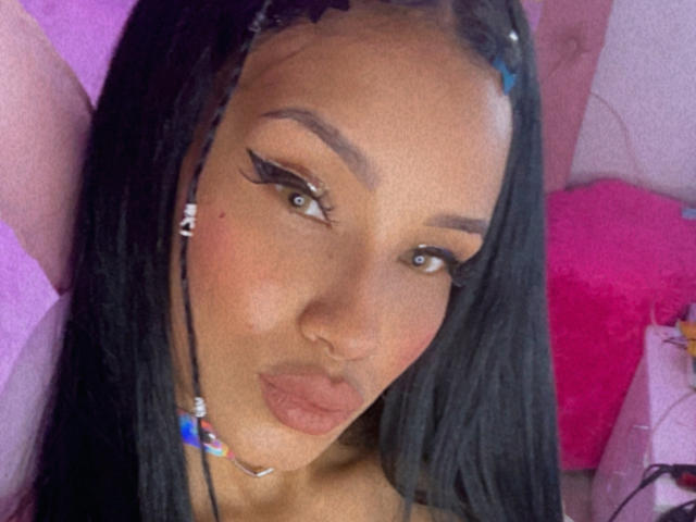 OnniOconor has dark brown skin, long black braids, and thick eyelashes with bold winged eyeliner. She has a nose ring and is pouting with her lips.