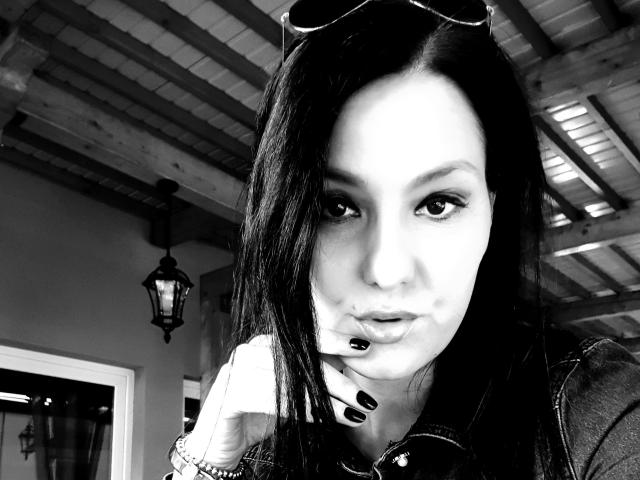 Black-and-white selfie of JoliDanielle with long dark hair, black lipstick, nose ring, and sunglasses on her head, looking at the camera with a slightly pouty expression.
