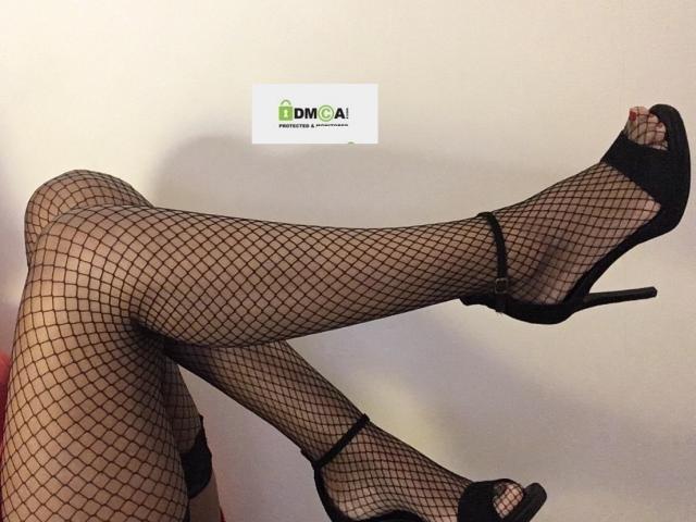 Le gambe di LaetitiaFun erano incrociate, indossava calze a rete nere e sandali con il tacco alto, mettendo in mostra le sue cosce e i suoi piedi, sensuali e formosi. La sua vulva è suggerita, ma non visibile..