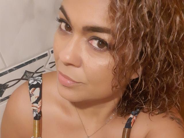 SolmaryHot ha i capelli ricci castano chiaro, gli occhi marroni e un sorriso delicato. Indossa un abito floreale con spalline dorate, che mette in mostra le spalle e un piccolo tatuaggio..