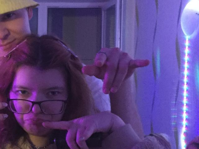 ChillOutt with red hair, glasses, and a pout, gets finger-pointed at by ChillOutt with a yellow hat, in a purple-lit room, showing a ring.