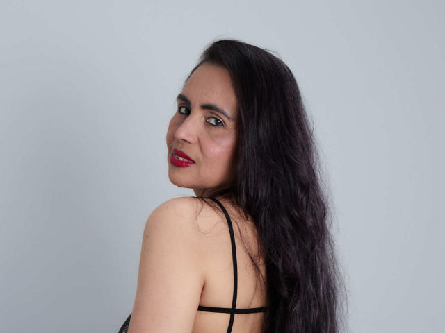 MoxiaHot has long, dark hair, red lipstick, and a slight smile, looking over her shoulder with black straps on her back. Her tits are visible. She's cute.